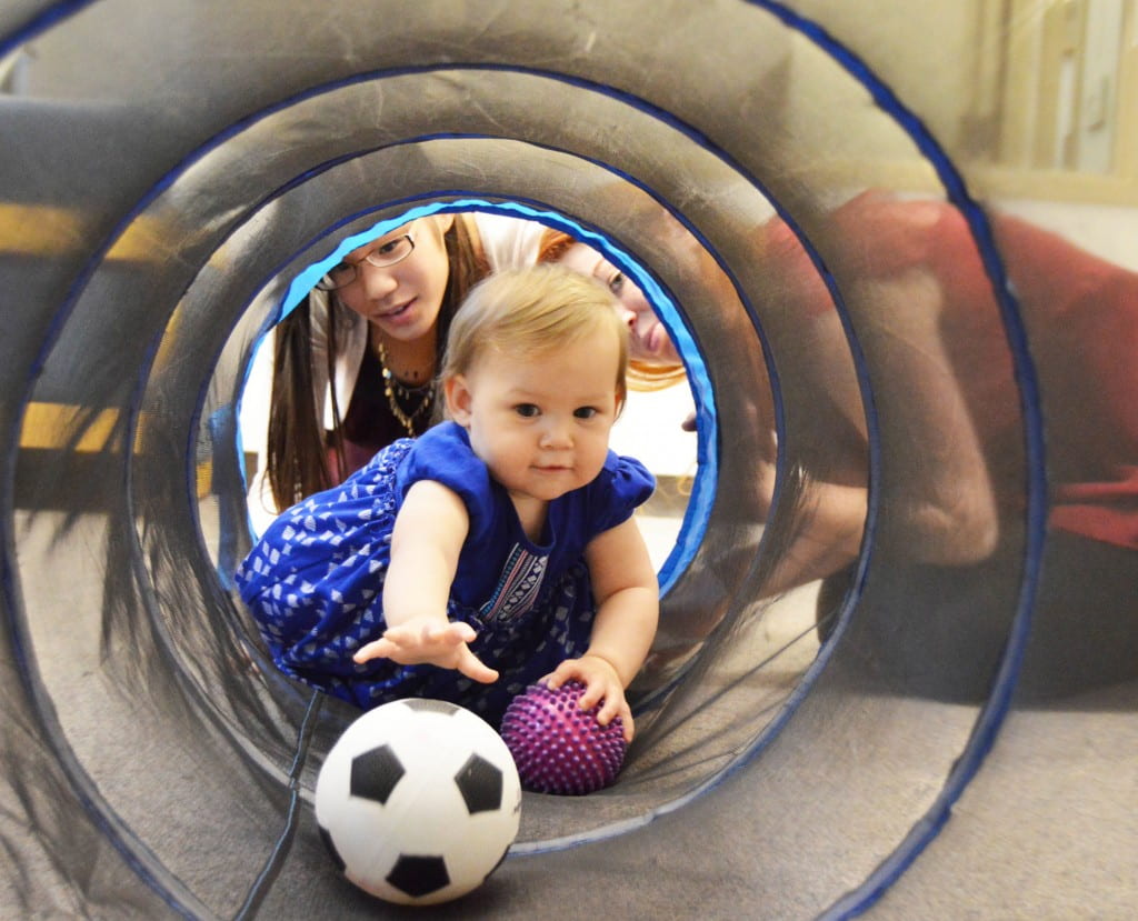 Researcher watches as a baby reaches for a ball inside a mesh tunnel.
